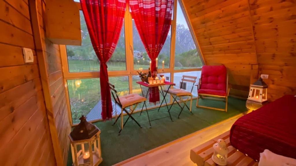 ein Schlafzimmer in einer Hütte mit roten Vorhängen sowie einem Tisch und Stühlen in der Unterkunft Bujtina Miqesia in Theth