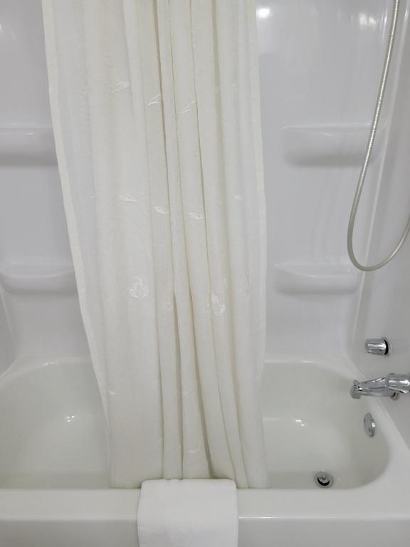 a shower with a white shower curtain in a bathroom at Husker Inn in North Platte