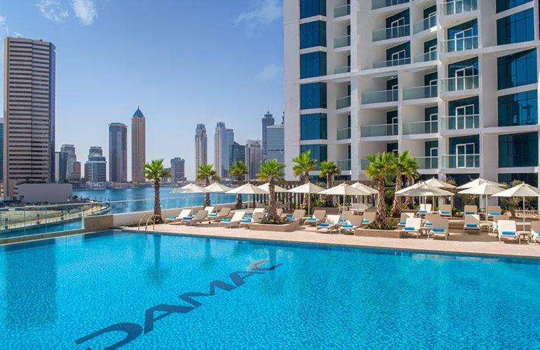 Damac Maison Prive Deluxe Studio with Burj-khalifa view في دبي: مسبح وكراسي ومظلات ومبنى