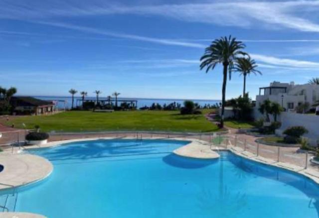 een groot blauw zwembad met palmbomen en de oceaan bij Villa Pedro, Beach House zwischen Marbella und Estepona in Estepona