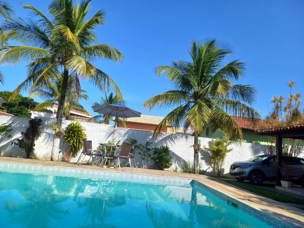 a swimming pool with palm trees and a house at Itaúna saquarema beach house in Saquarema