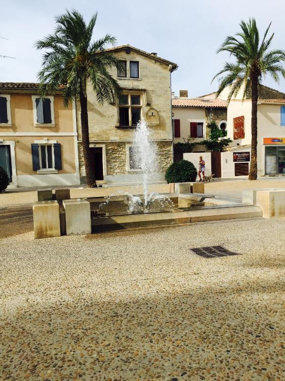 une fontaine en face d'un bâtiment avec des palmiers dans l'établissement La maison sur la place dans la vieille ville Aigues Mortes, à Aigues-Mortes