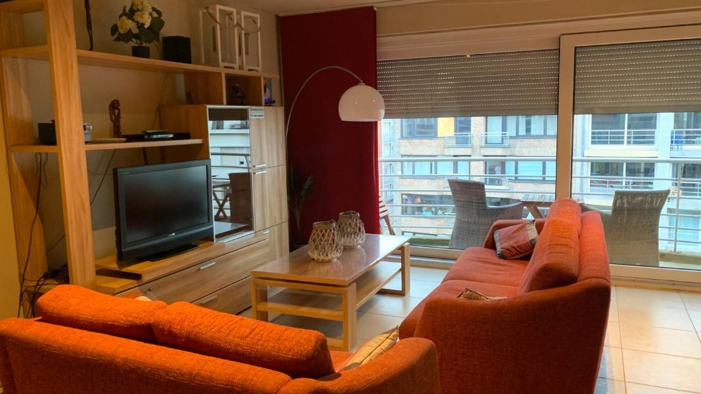 ein Wohnzimmer mit 2 orangenen Stühlen und einem TV in der Unterkunft Appartement “zon en vakantie aan zee” in Koksijde