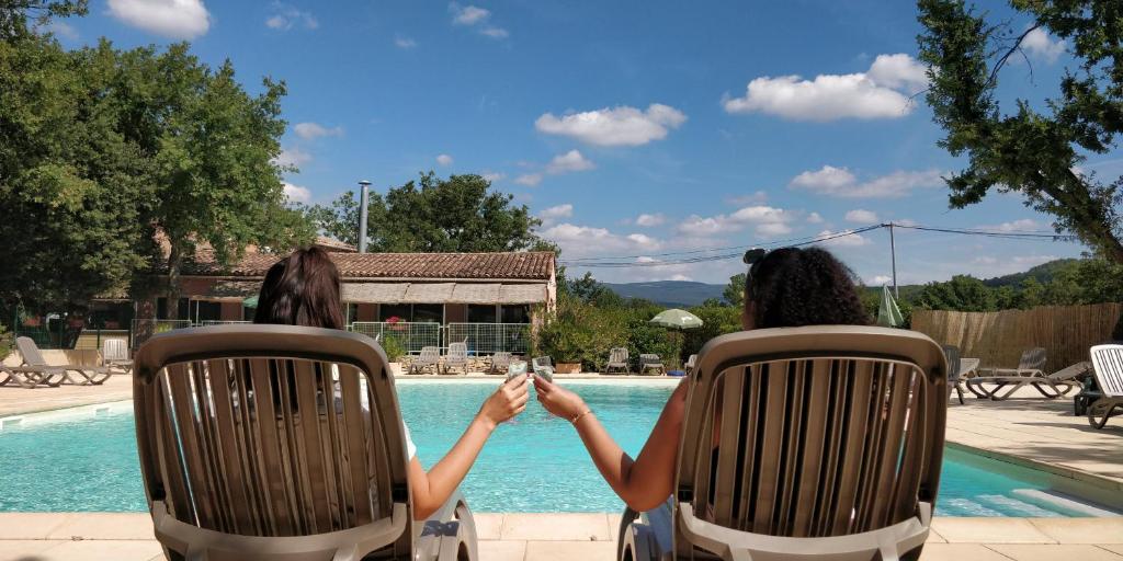 dos mujeres sentadas en sillas junto a una piscina en Domaine Les Chênes Blancs, en Saint-Saturnin-lès-Apt