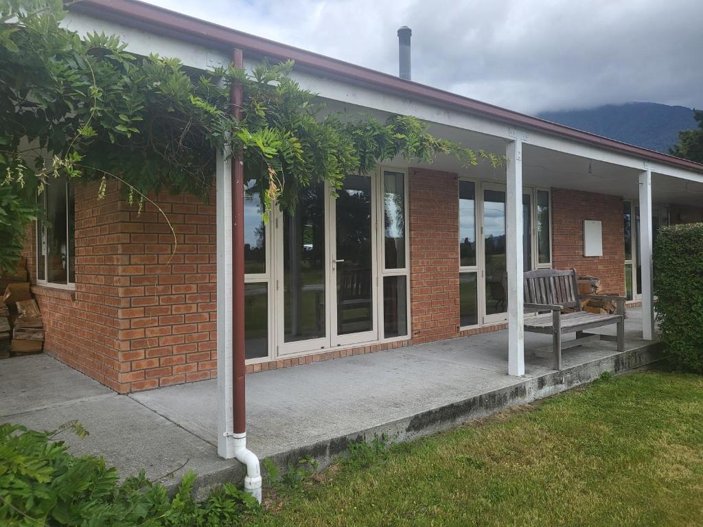 ein Backsteingebäude mit einer Bank auf einer Veranda in der Unterkunft Misty Peaks Guesthouse in Fox Glacier