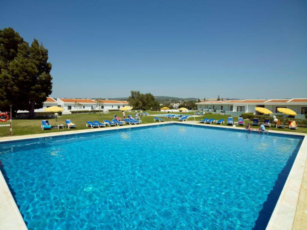 a large blue swimming pool with chairs and a building at Hotel Apartamento Do Golfe in Vilamoura