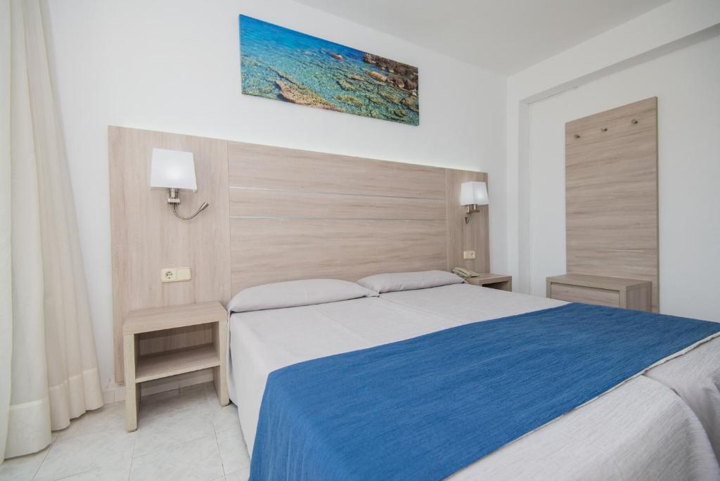 a bedroom with a large bed with a blue blanket at Hotel Bella Mar in Cala Ratjada