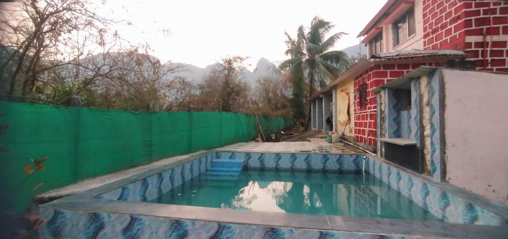 a swimming pool next to a house with a green fence at Weekend Villa at Nature's Lap (Malshej Ghat) in Ghātghar