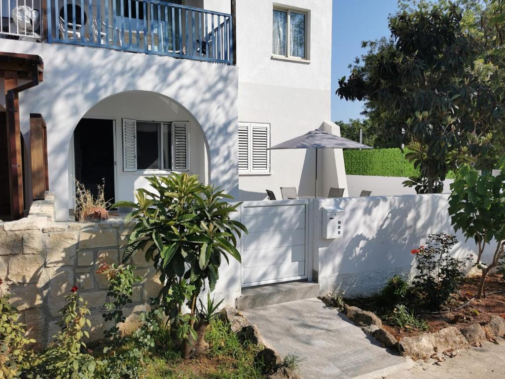 a white house with a fence and an umbrella at Paphos Gardens Apartment in Paphos City