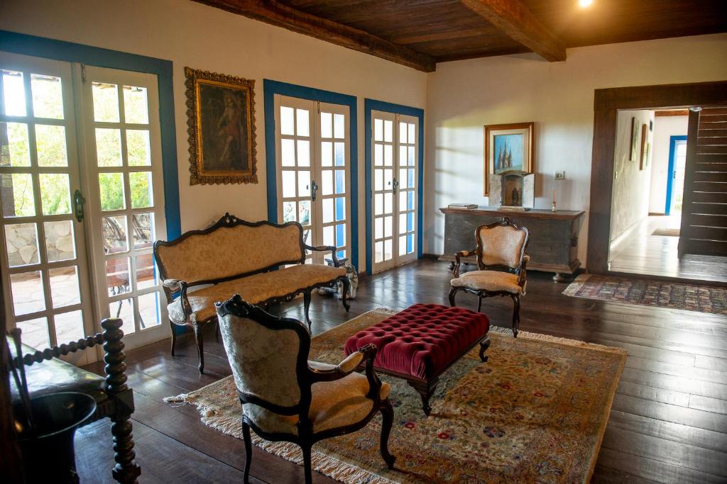 a living room with chairs and a table and windows at Casarão Milho Verde in Milho Verde