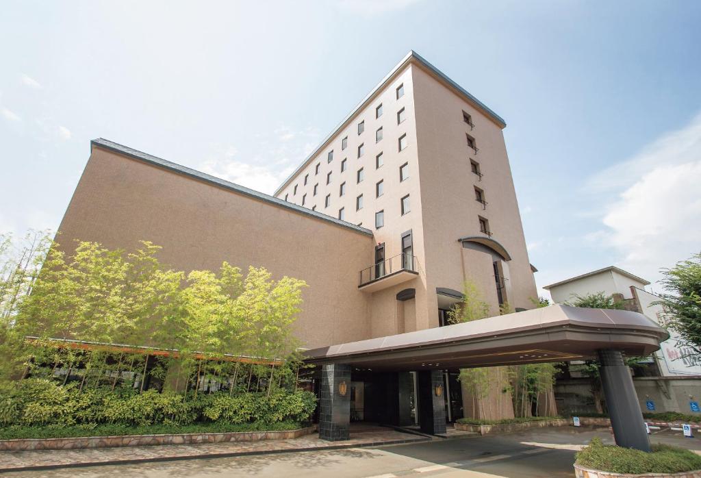 um grande edifício branco com um guarda-chuva em frente em Yonezawa Excel Hotel Tokyu Reopening on June 1 "DEN'S HOTEL yonezawa" em Yonezawa