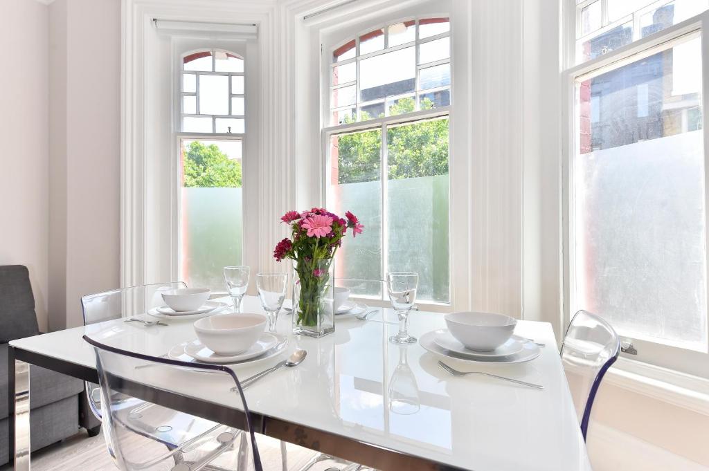 a white dining room with a table with flowers on it at Paddington Gardens in London