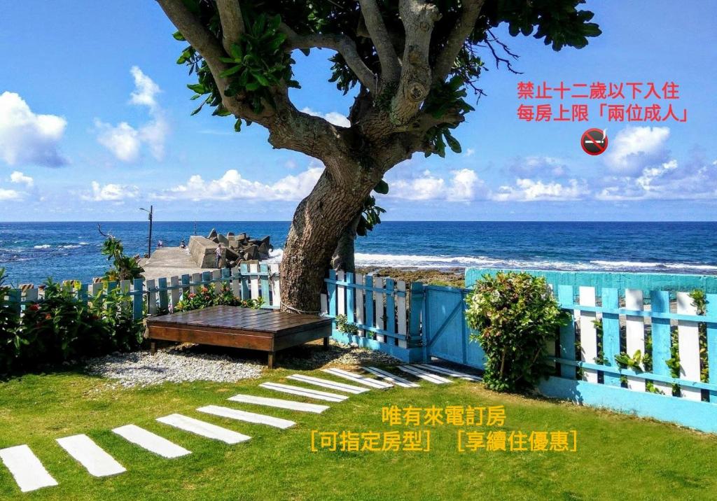 a bench sitting under a tree next to the ocean at 灣境海邊小屋 in Eluan