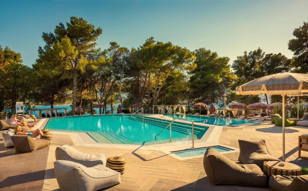 a swimming pool with chairs and umbrellas in front at HVAR PLACESHOTEL by Valamar in Stari Grad