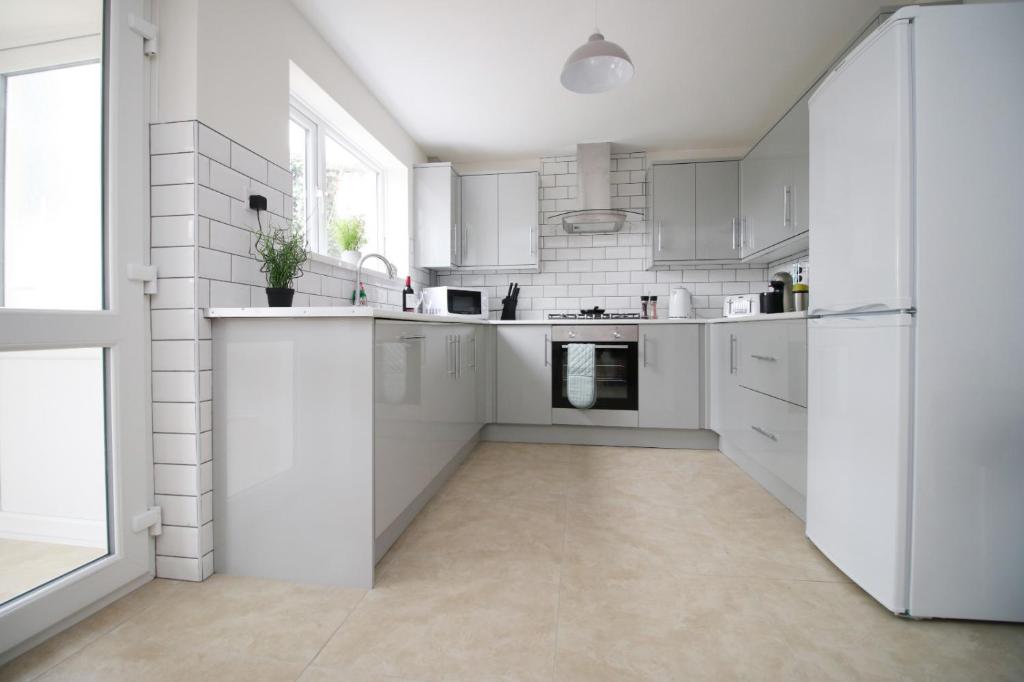 a white kitchen with white appliances and a large window at Family Home in the Charming Coastal Town of Barry in Barry