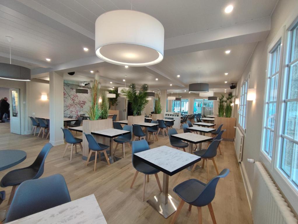 a restaurant with tables and chairs and windows at Le Relais des Primeurs LOGIS HOTEL in Taulé