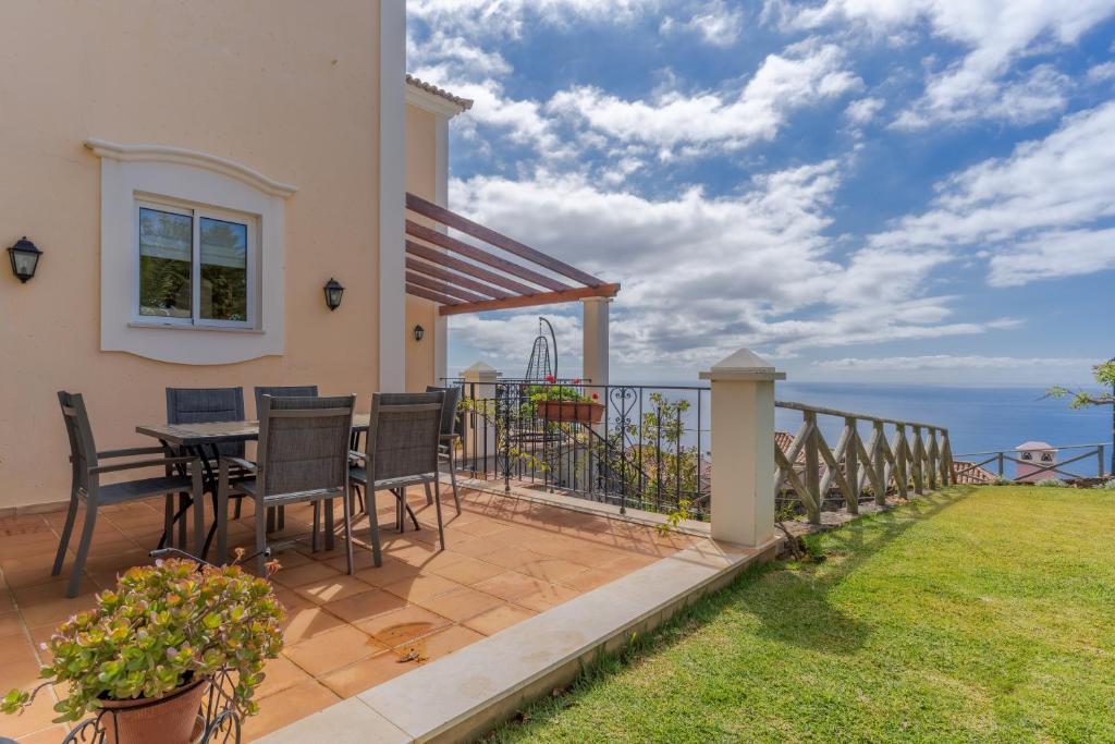 Villa Bougainvillea Palheiro Village by HR Madeira في فونشال: منزل مع شرفة مع طاولة وكراسي