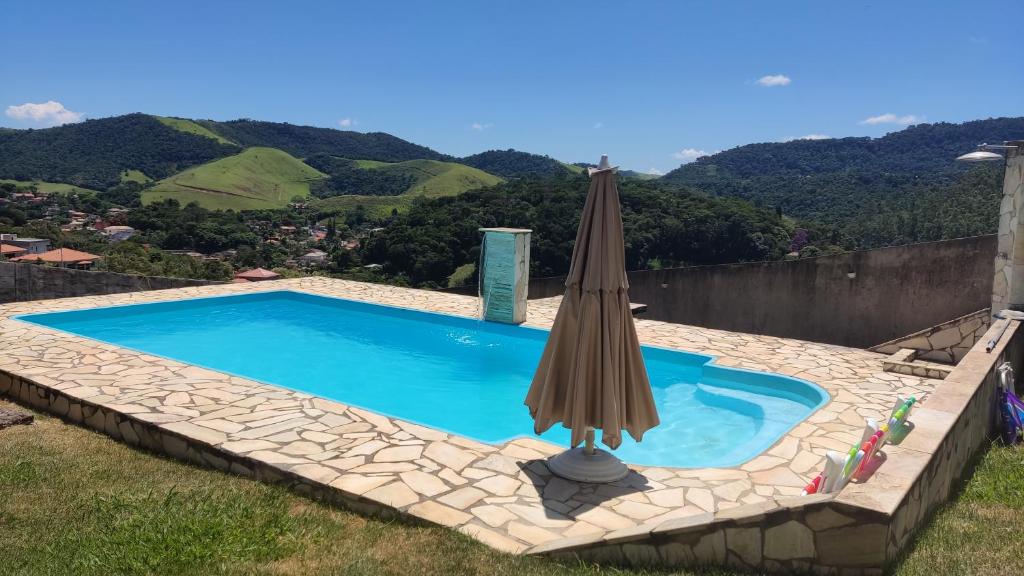 a blue swimming pool with an umbrella and a hill at Suite Requinte da Serra in Miguel Pereira