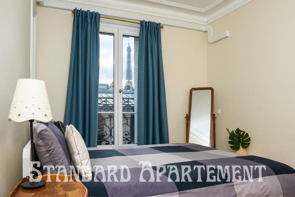 a bedroom with a bed with blue curtains and a window at Eiffel Tower view Residence in Paris