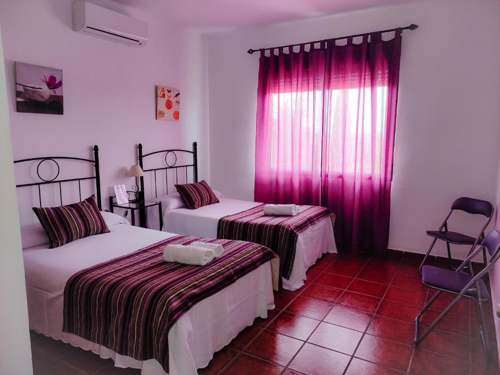 Habitación con 2 camas y ventana con cortinas rosas. en Casa Rural La Aduana, en Villanueva del Fresno