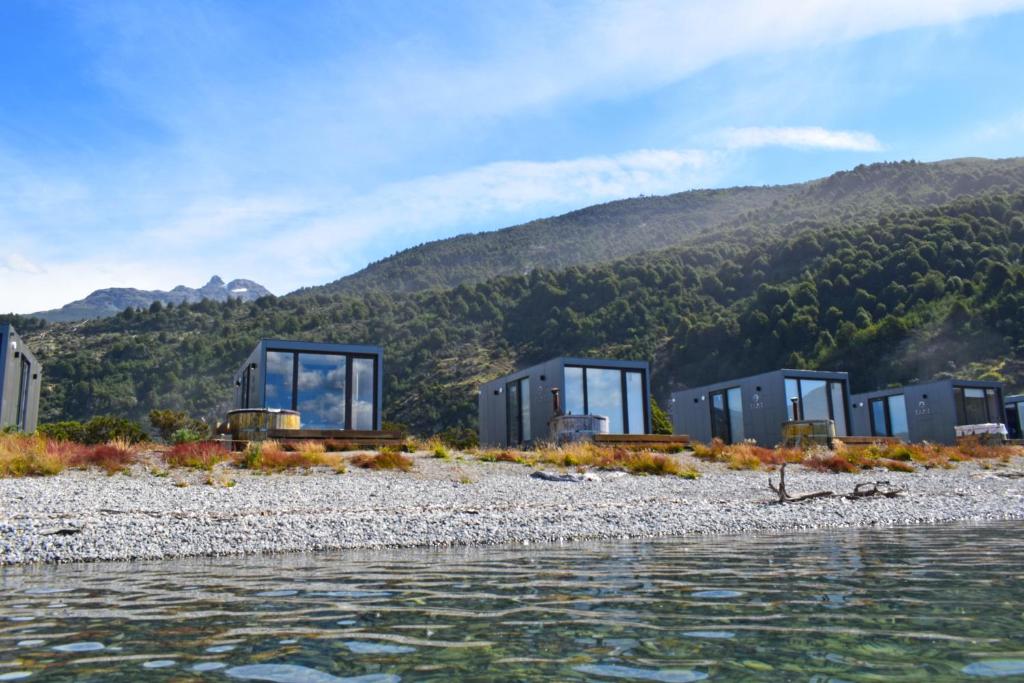 a row of glass buildings on a beach next to the water at Chelenko Lodge in Puerto Tranquilo