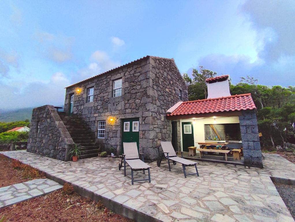 een klein stenen huis met 2 stoelen en een patio bij Adega da Prainha in Prainha de Baixo