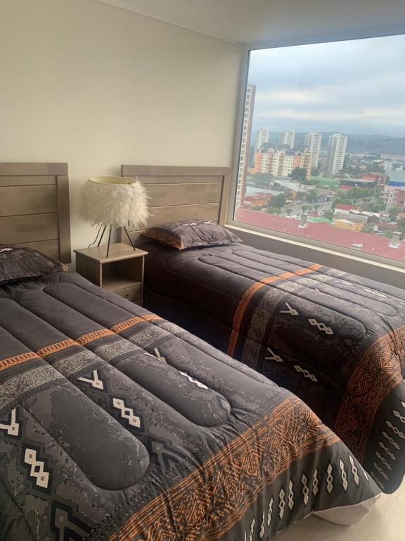 two beds in a room with a large window at Piso 13 Concepcion in Concepción