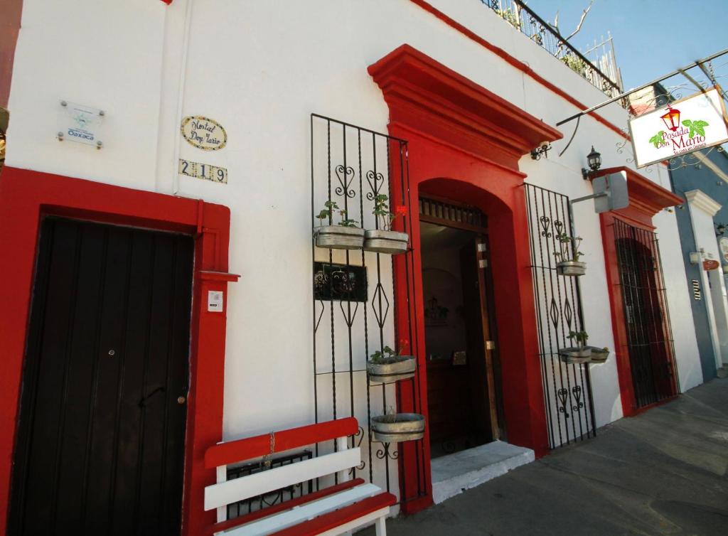 ein rot-weißes Gebäude mit einer Tür und einer Bank in der Unterkunft Posada Don Mario in Oaxaca de Juárez