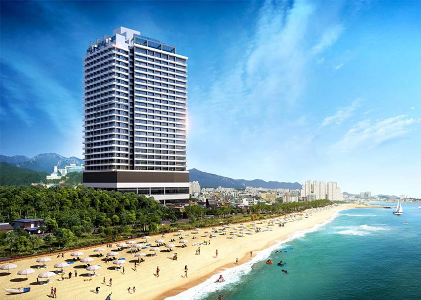 a beach with people and umbrellas and a tall building at Hotel The Blue Terra in Sokcho
