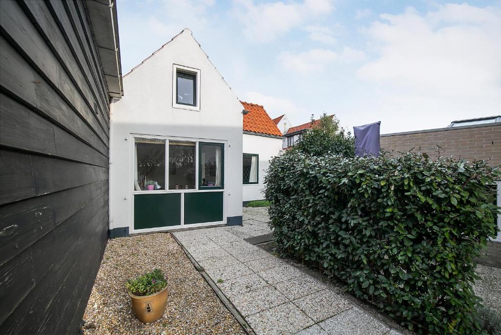 een wit huis met groene deuren en een heg bij Hello Zeeland - Vakantiehuis Beatrixstraat 27A in Domburg