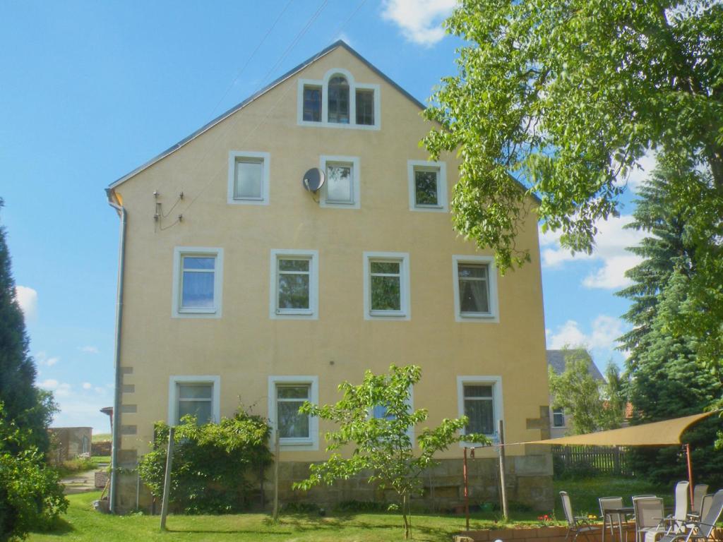ein großes gelbes Haus mit weißen Fenstern und einem Baum in der Unterkunft Ferienwohnung Am Lindenbaum in Kirnitzschtal