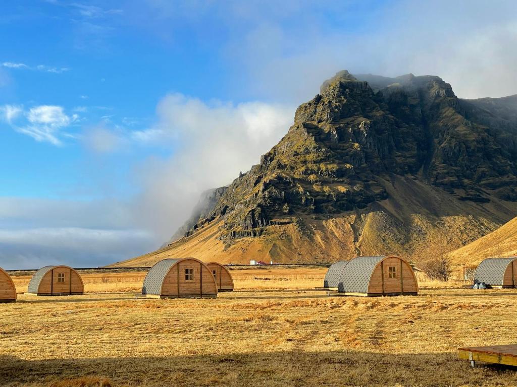 a group of wooden buildings in front of a mountain at Starlight Camping Pods in Hvolsvöllur