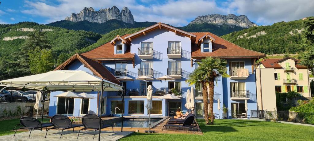 un hôtel dans les montagnes avec des chaises et des parasols dans l'établissement Hôtel Le Mouton Bleu, à Talloires