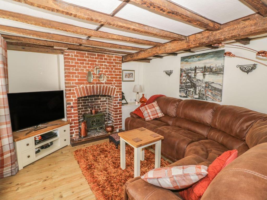 a living room with a leather couch and a fireplace at Chapel Cottage in Pewsey