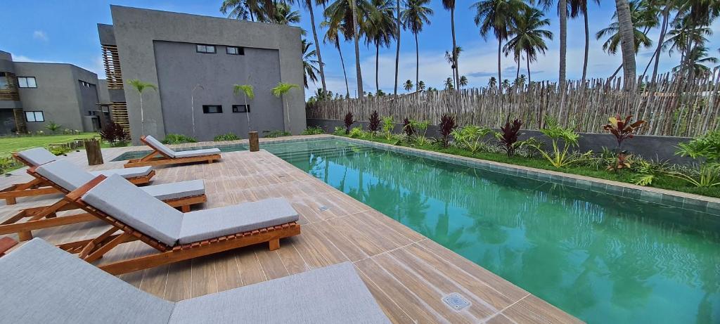 a swimming pool with two lounge chairs and a house at Praia do Patacho - Milagres in Pôrto de Pedras