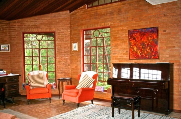 uma sala de estar com cadeiras laranja e um piano em Casa aconchegante na montanha à 15min do centro! em Campos do Jordão