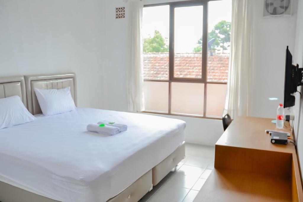 um quarto com uma grande cama branca e uma janela em Bumi Ciboled Mitra RedDoorz near Gerbang Tol Pamulihan em Jatinangor