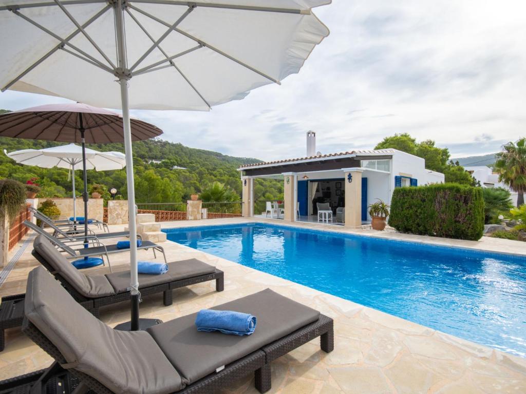 a villa with a swimming pool with two chairs and an umbrella at Holiday Home Anromi by Interhome in Cala Vadella
