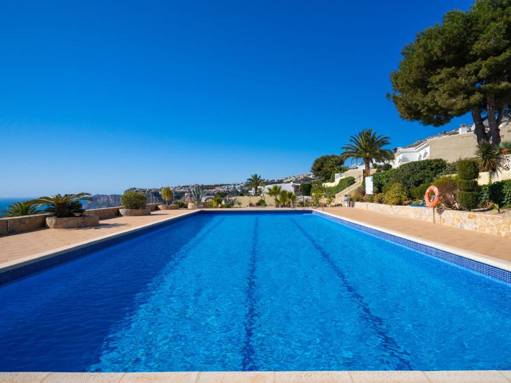 - une piscine d'eau bleue avec des arbres et l'océan dans l'établissement Holiday Home Pueblo de la Luz by Interhome, à Cumbre del Sol