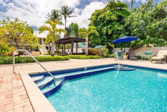 einen Pool mit Sonnenschirm neben einem Haus in der Unterkunft Beach Living at Island Pine Villas BLAW in George Town