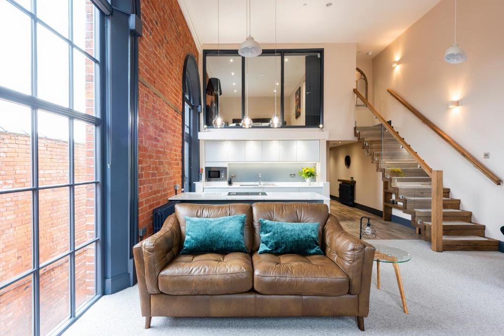 a living room with a brown leather couch in front of a brick wall at The Old Chapel Apartments in Edwinstowe