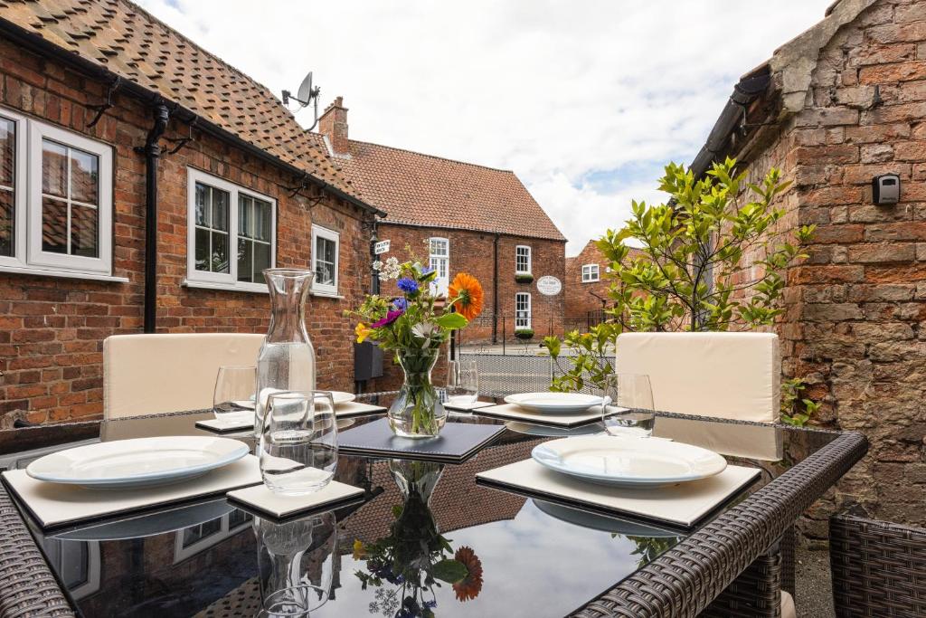 a glass table with plates and flowers on a patio at Ropemaker’s Cottage in Ollerton