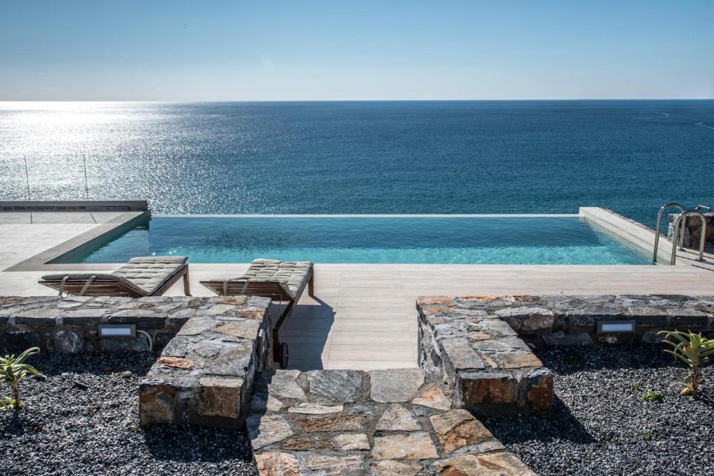 a pool with chairs and the ocean in the background at Evgoro - Infinite View in Tsoútsouros