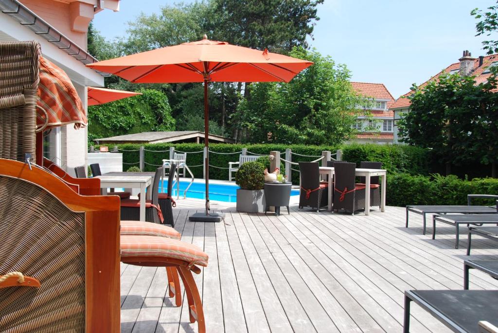 eine Terrasse mit einem Sonnenschirm, Tischen und Stühlen in der Unterkunft Hotel Rubens in De Haan