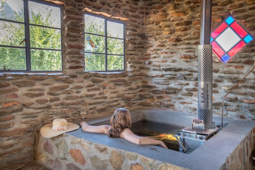 Una donna seduta in una vasca da bagno in un muro di pietra di Lank-gewag Farm Cottage with private hottub a Montagu