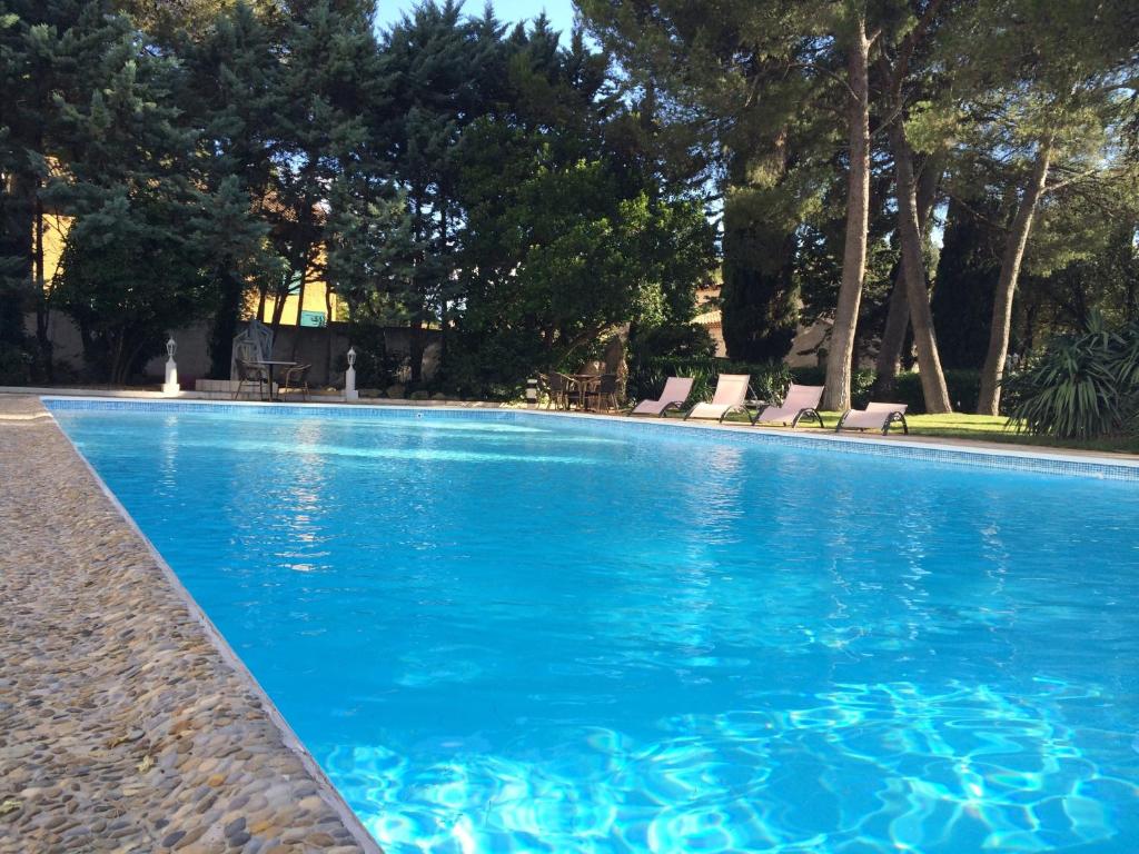 ein blauer Pool mit Stühlen und Bäumen in der Unterkunft Cit'Hotel Le Mirage in Istres