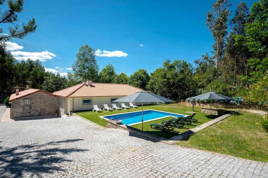 una casa con piscina con sillas y sombrillas en Casa do Pioledo Camélias de Basto en Lamelas