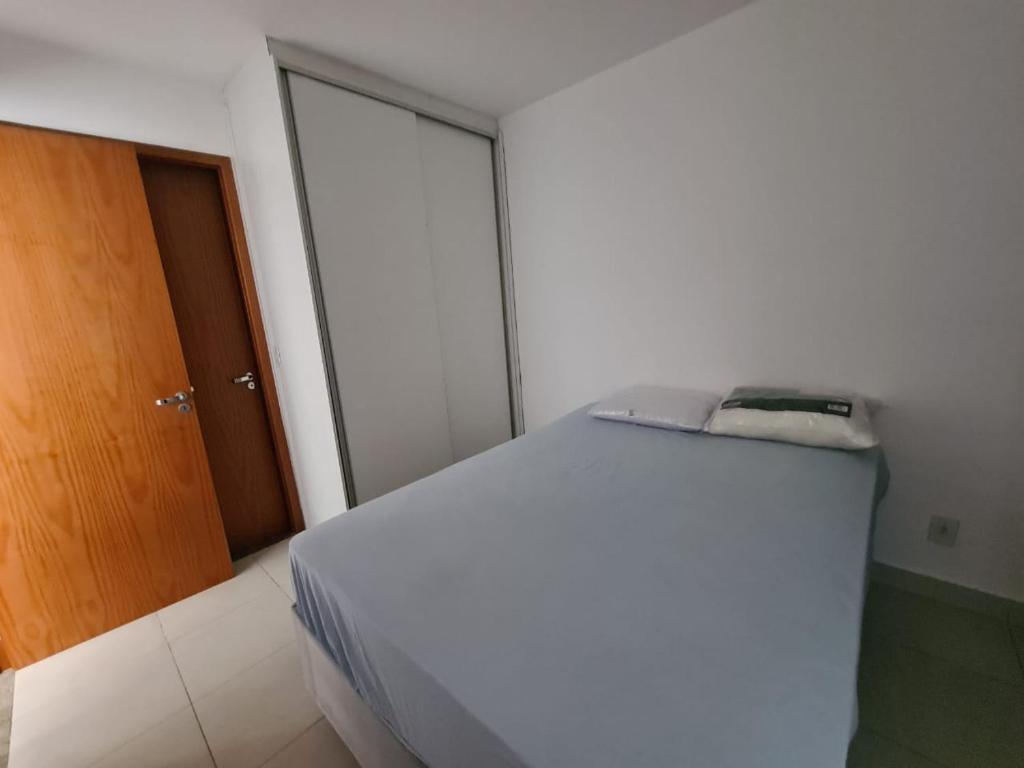 een slaapkamer met een wit bed en een houten deur bij Apt encantador: piscina, academia, tela proteção in Taguatinga