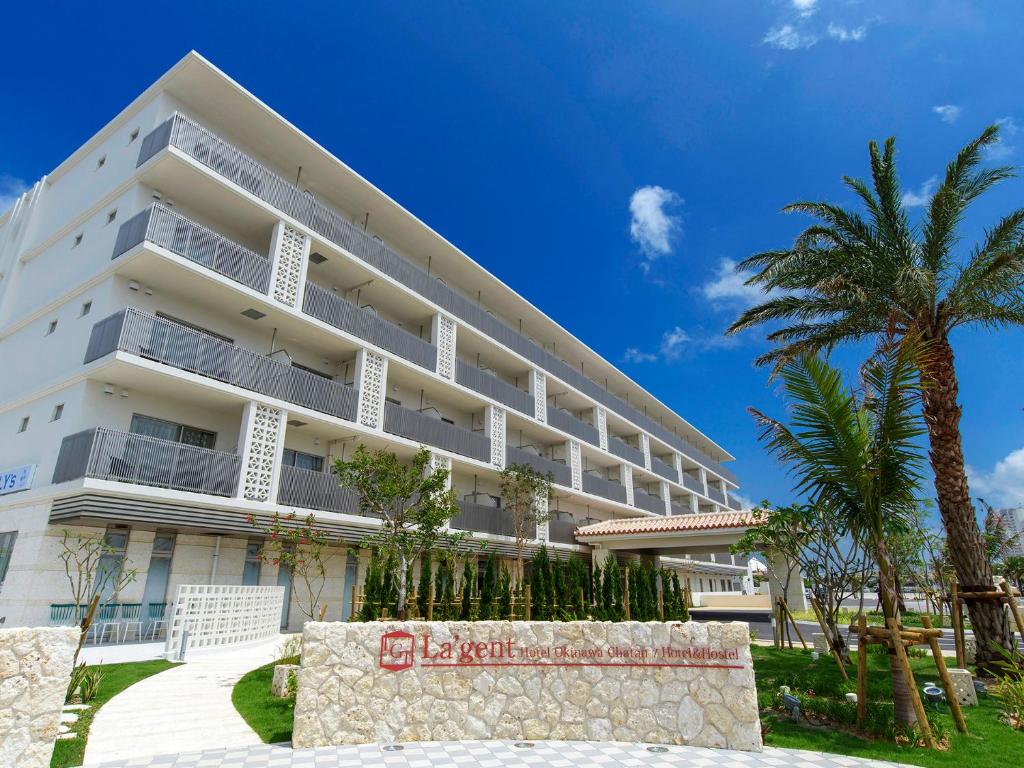 a large white building with palm trees in front of it at La'gent Hotel Okinawa Chatan Hotel and Hostel in Chatan