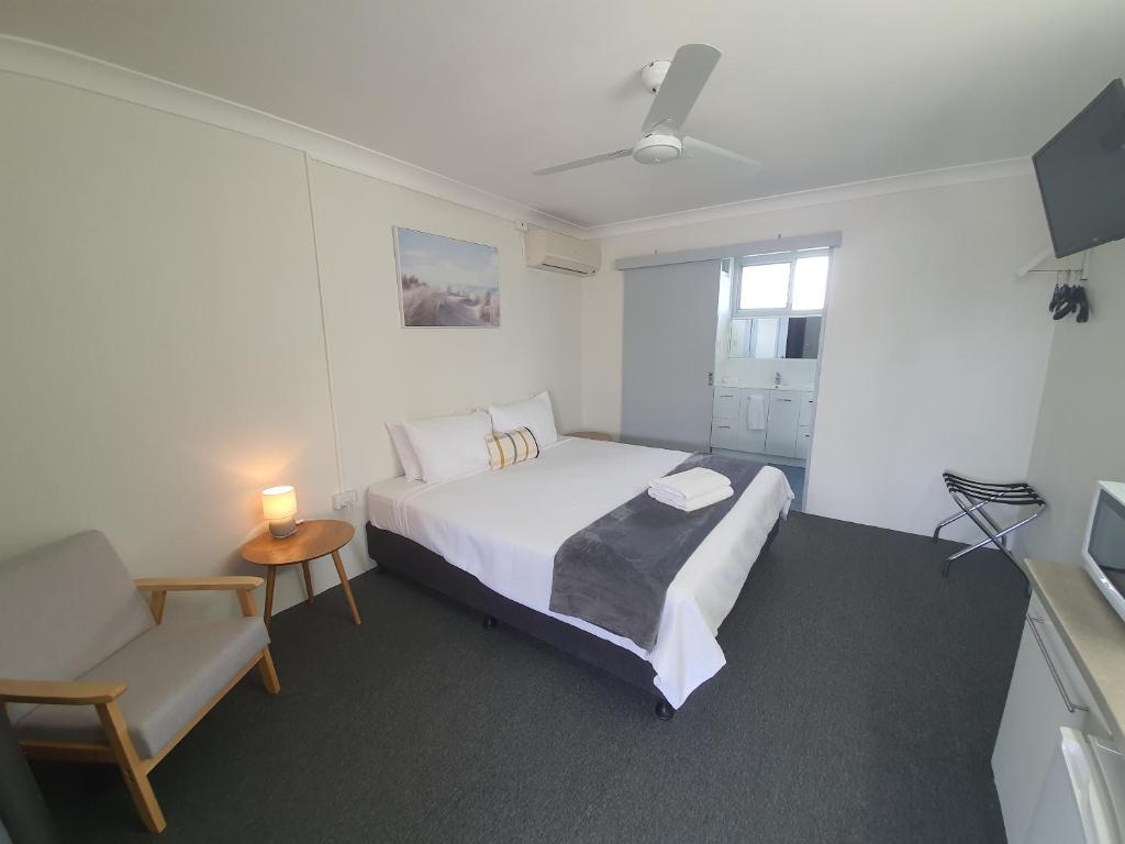 um quarto com uma cama branca e uma cadeira e uma cama sidx sidx sidx em Sun City Motel em Bundaberg